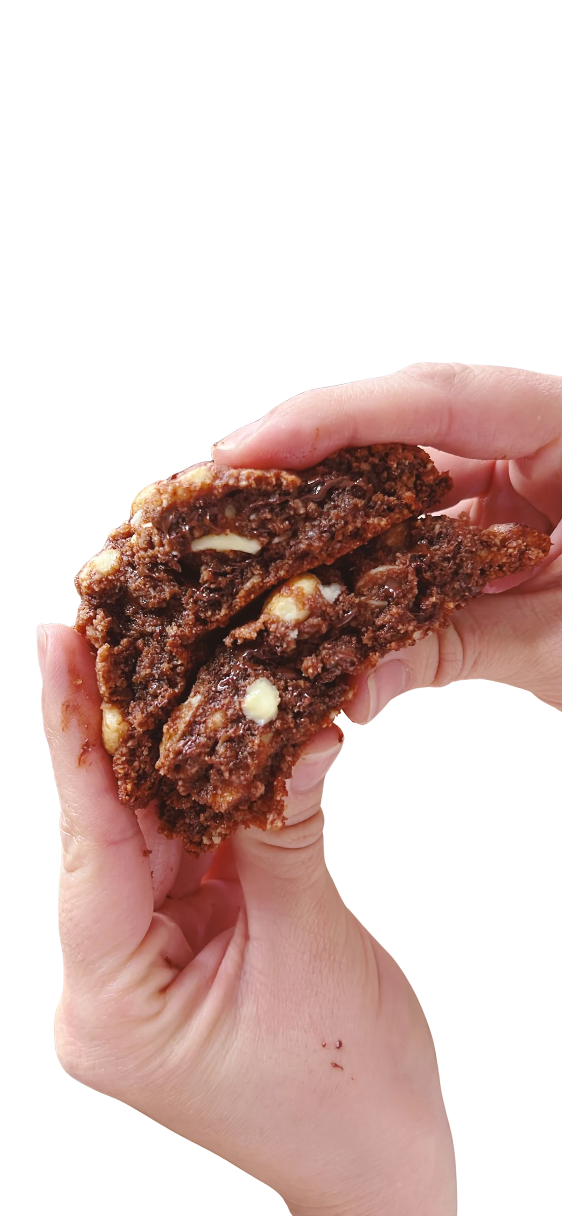 Galleta keto de doble chocolate partida en la mano, con trozos de chocolate blanco y negro visibles en la miga oscura
