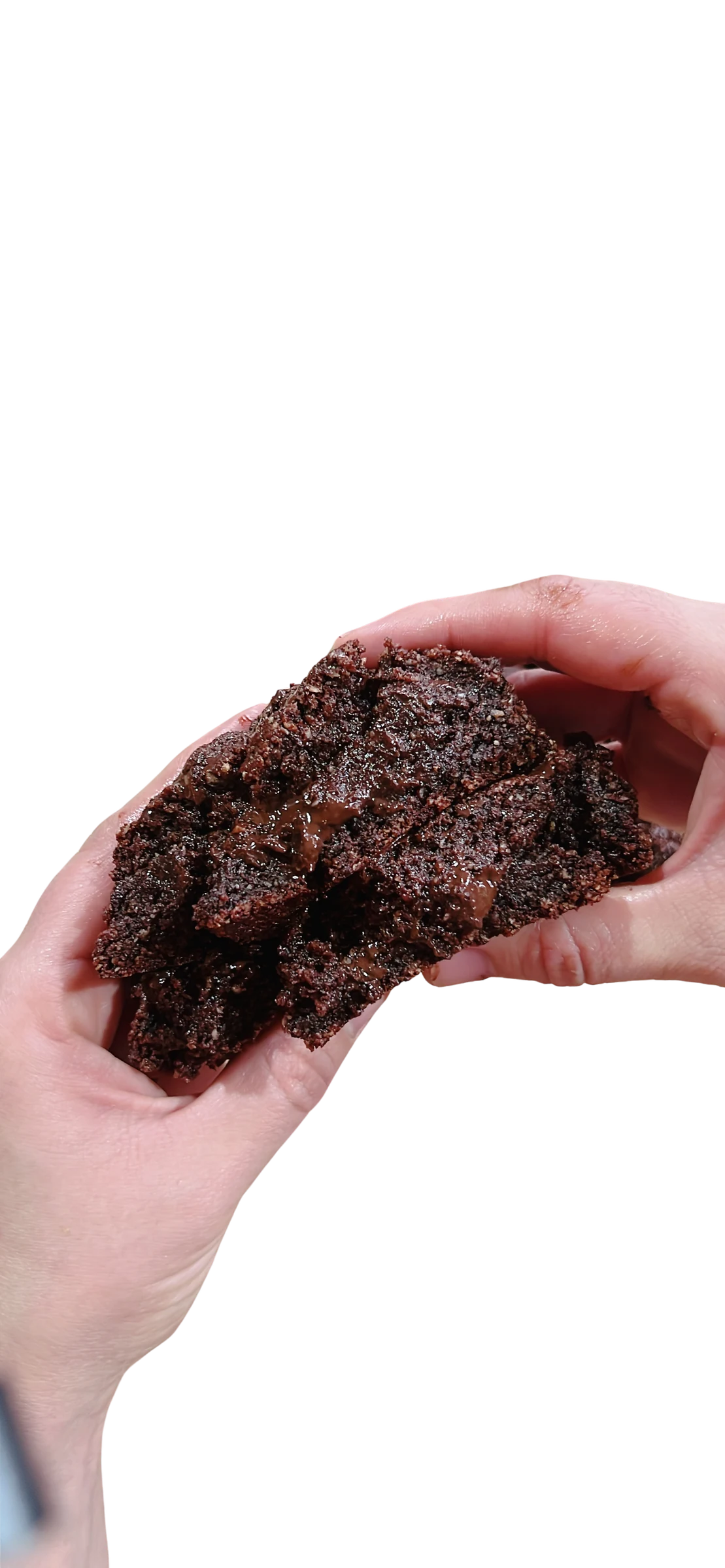 Galleta keto de brownie partida en la mano, con miga húmeda y muy oscura