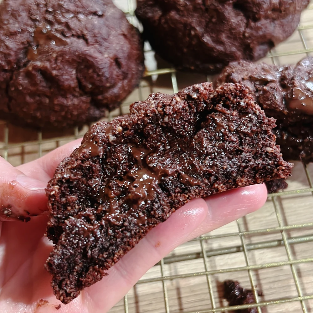 Galleta keto de brownie partida en la mano, con miga húmeda y muy oscura