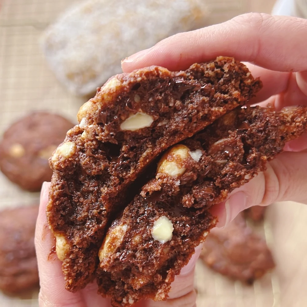 Galleta keto de doble chocolate partida en la mano, con trozos de chocolate blanco y negro visibles en la miga oscura