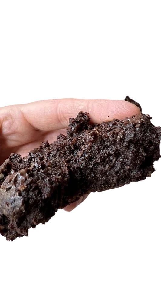 Galleta keto de chocolate negro y menta de miga muy oscura sostenida entre los dedos