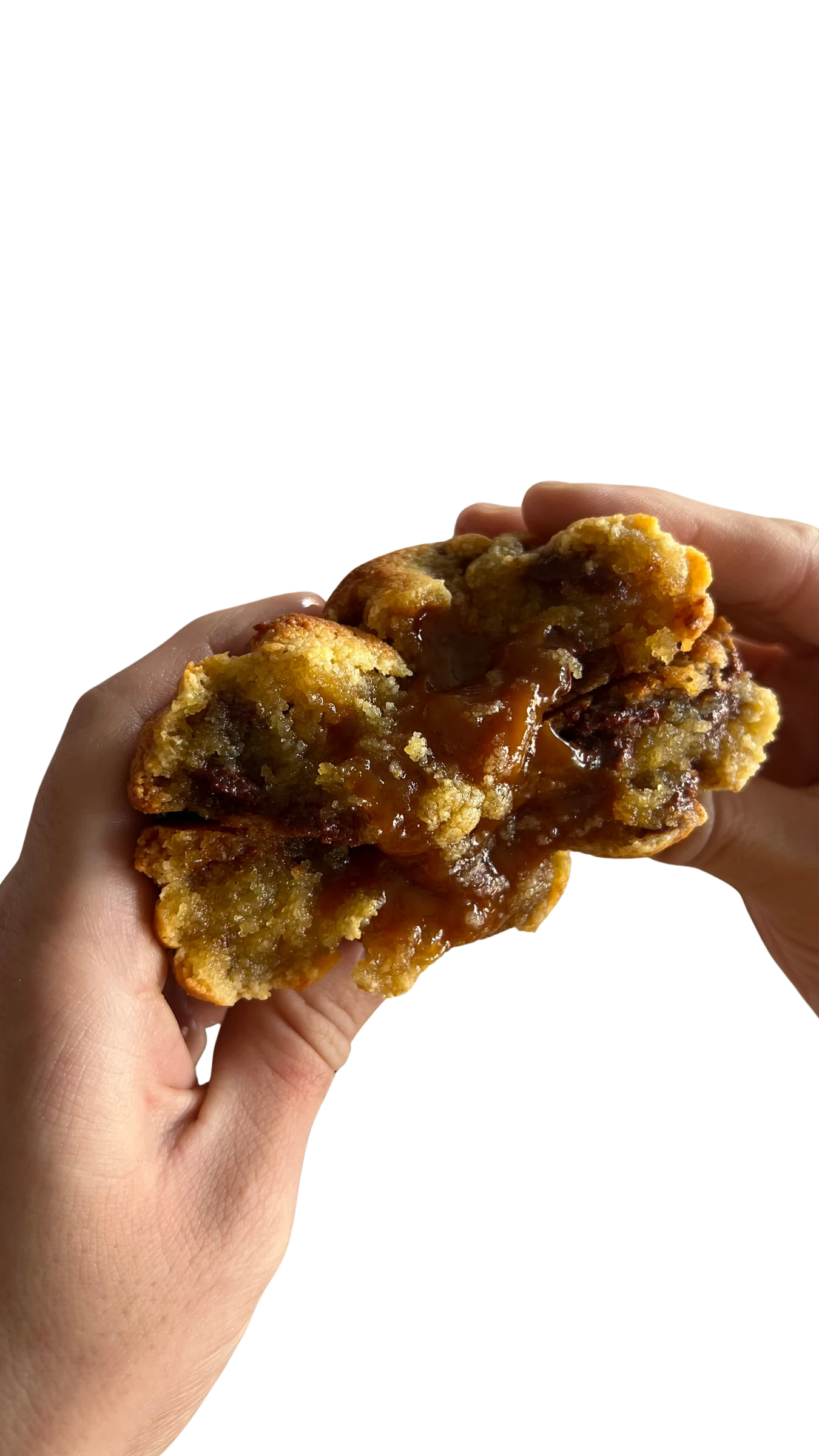 Galleta keto de caramelo salado sostenida en la mano y partida, con el caramelo escurriendo desde el centro